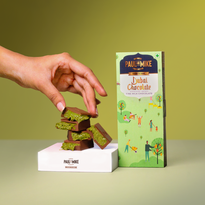 Hand holding Paul & Mike Kunafa Pistachio Chocolate – creamy Dubai-style chocolate with kataifi and 70% pistachio filling, pastel green backdrop.